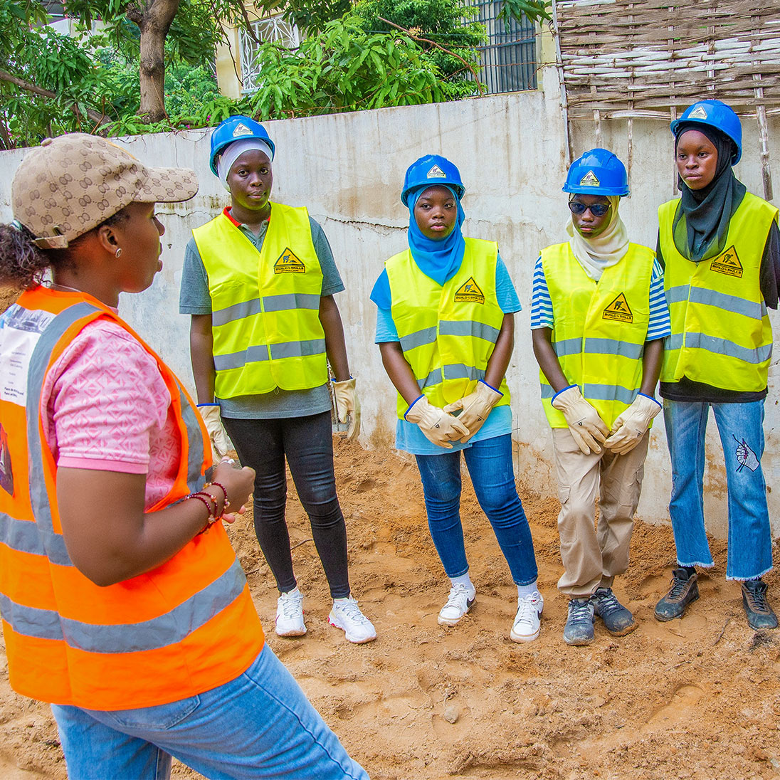Group photo with Djélia Diagne (in profile on the left) talking to five young women in hard hats and high-visibility vests on a construction site.